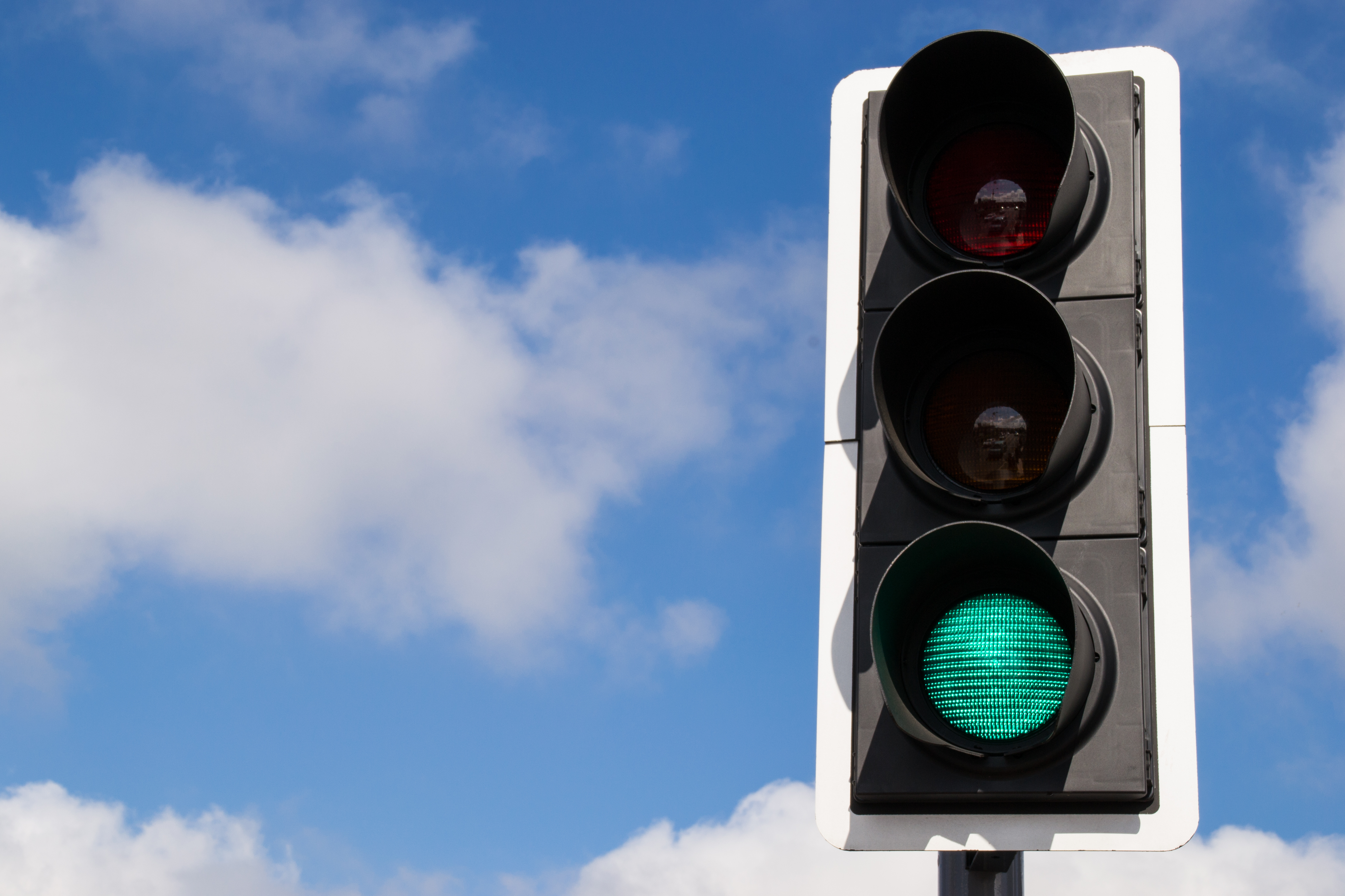 A green traffic light against a blue sky with a few fluffy white clouds. Image by Eddie J. Rodriquez via Shutterstock.