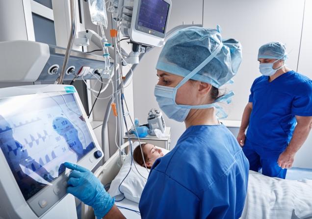 A healthcare worker working at a machine in an intensive care unit. Image by Peakstock via Shutterstock.