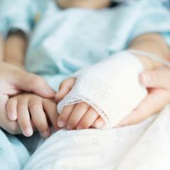 Image by Kunlathida6242 via Shutterstock. Close-up of a parent holding the hands of a child in a hospital - the child's hand is bandaged and has a drip. Image by Kunlathida6242 via Shutterstock.