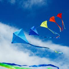 Image by Sergey Novikov via Shutterstock. A string of coloured kites flying high against a blue sky with a few white clouds. Image by Sergey Novikov via Shutterstock.