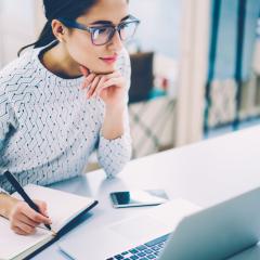 Image by GaudiLab via Shutterstock A woman looking at a computer screen and taking notes.